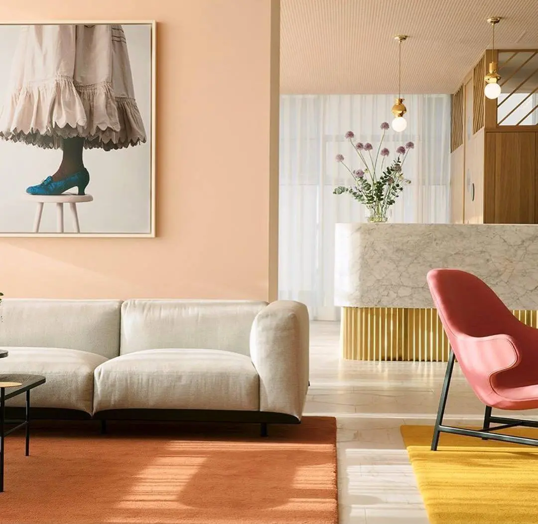 white sofa on orange rug with a pink wall and art and flowers