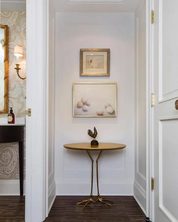 Entryway nook with an oval console table on slender bird-shaped brass legs and framed art