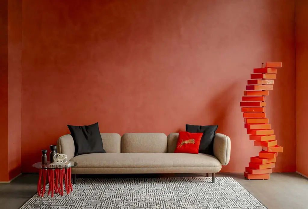 Terracotta living room with beige sofa, black pillows and a sculptural stacked-block totem