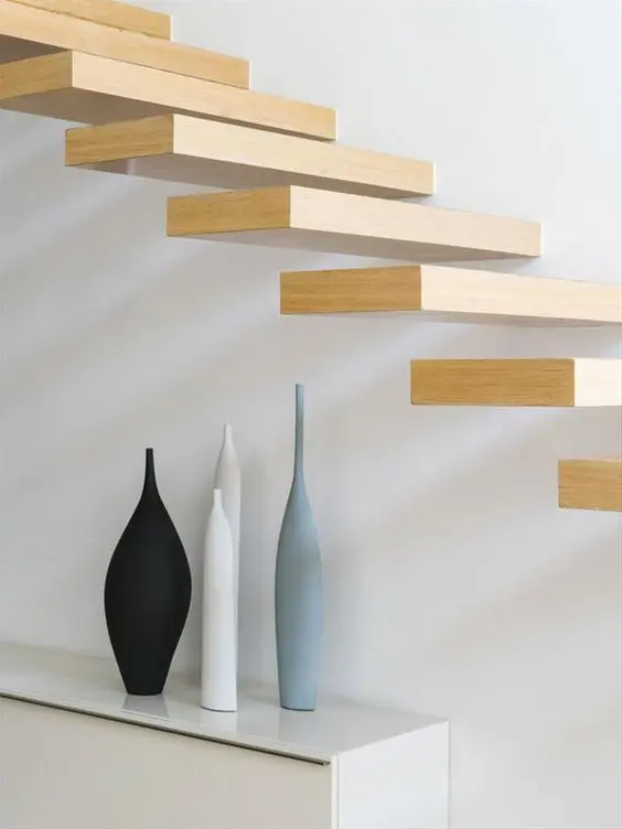 Floating wood staircase steps with three tapered ceramic vases on a white console