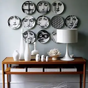 Wall of black and white face-motif decorative plates above a wood console table