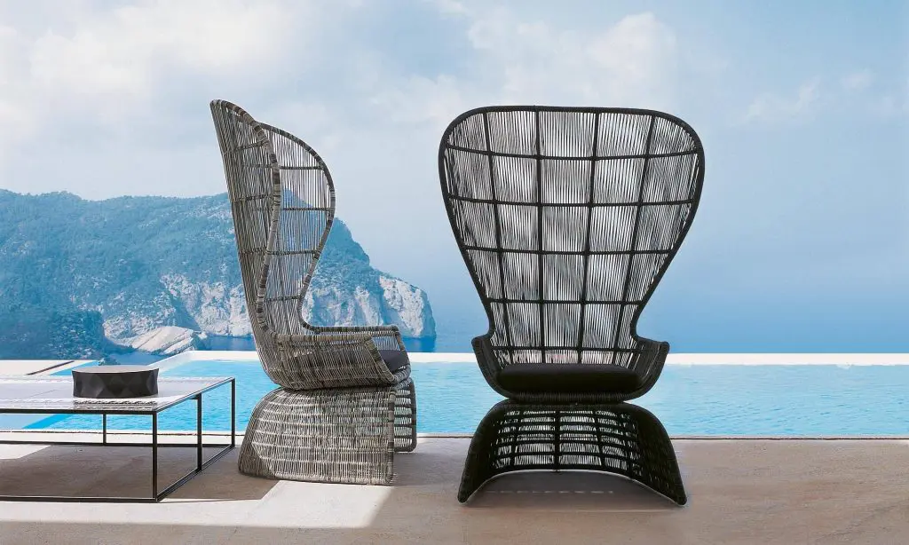 Black high-backed wicker lounge chairs on a terrace overlooking a cliff and the sea