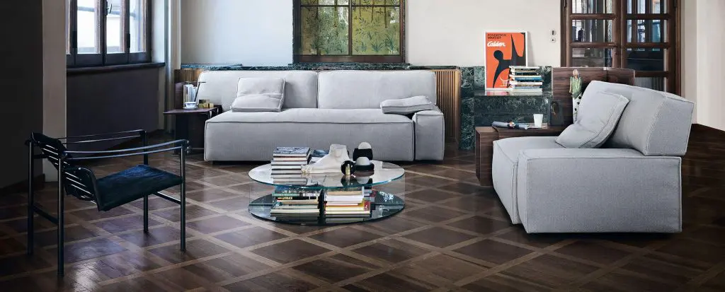 Cassina living room with a light grey modular sofa, round glass coffee table and a black leather chair on parquet