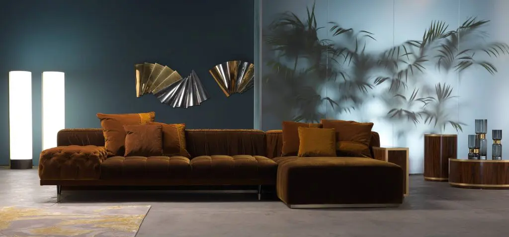 Gianfranco Ferré Home living room with a rust velvet tufted sectional sofa against teal walls and gold fan-shaped wall art