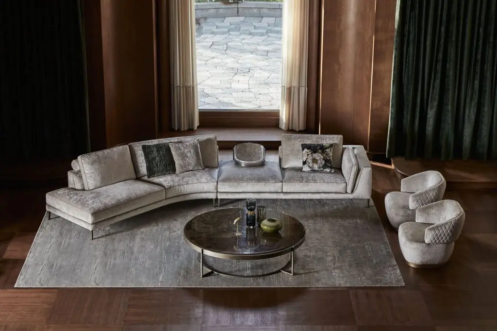 Living room with a curved beige velvet sofa, black-framed arched windows and a marble fireplace