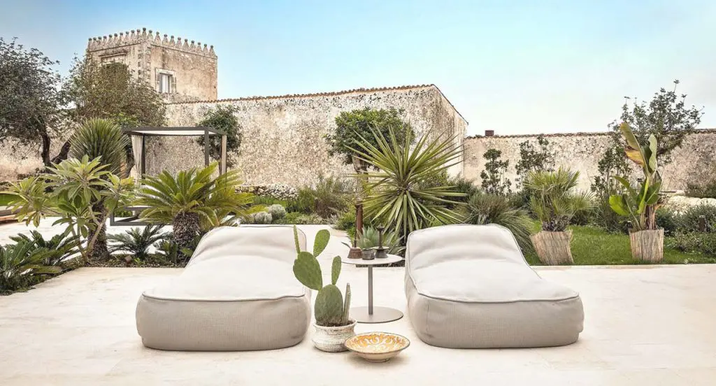 Two cream bean bag loungers on a stone terrace with cacti, palms and a stone tower in the background