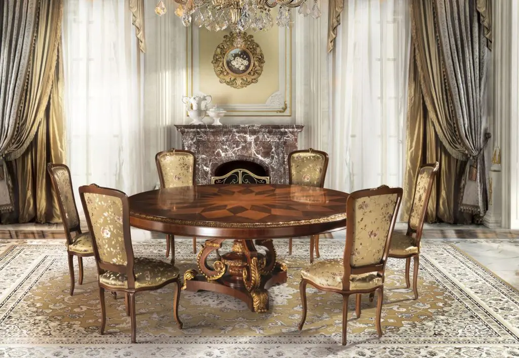 Classic dining room with a round wood table, gold-upholstered chairs, chandelier and marble fireplace