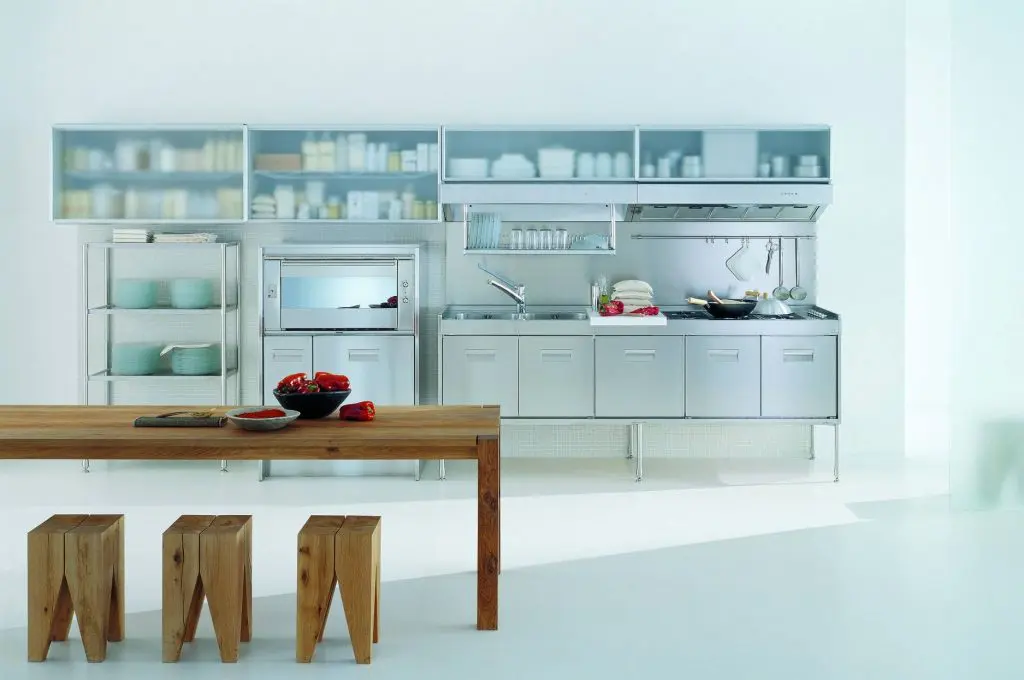 Arclinea stainless steel kitchen with glass cabinets and a wood table with block stools