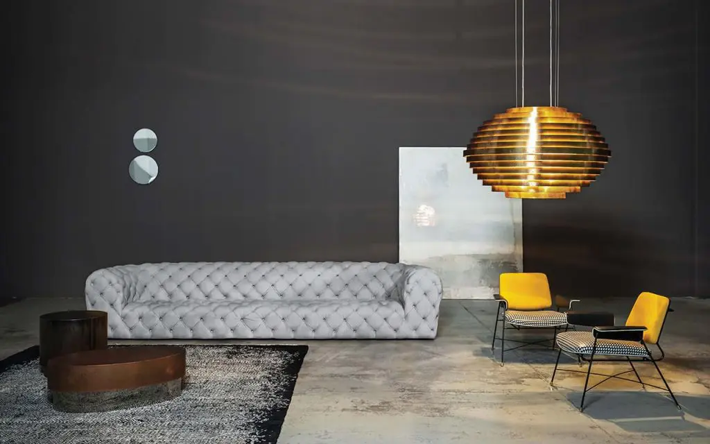 Contemporary living room with a grey tufted chesterfield sofa, gold shell pendant light and yellow houndstooth armchairs