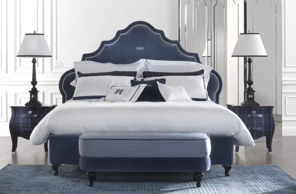 Gianfranco Ferré Home bedroom with a navy tufted headboard bed, dark wood nightstands and a mirrored wall