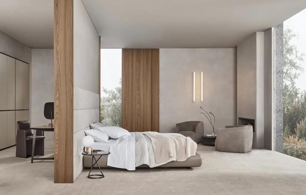 Poliform bedroom with a low upholstered bed, wood panel wall and swivel armchairs beside a fireplace