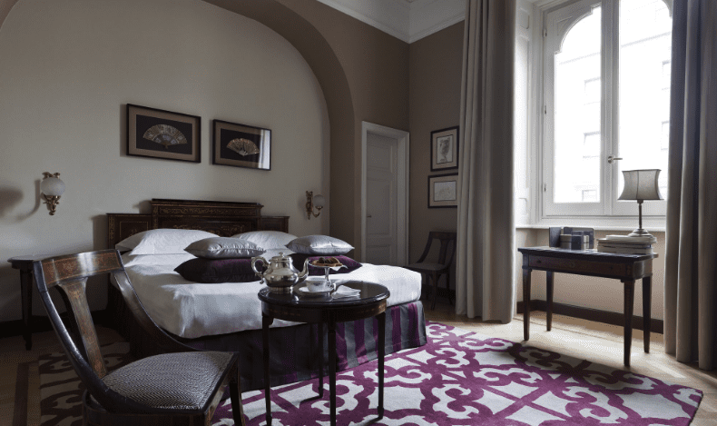 Hotel bedroom with a patterned purple rug, arched doorway and a canopy bed