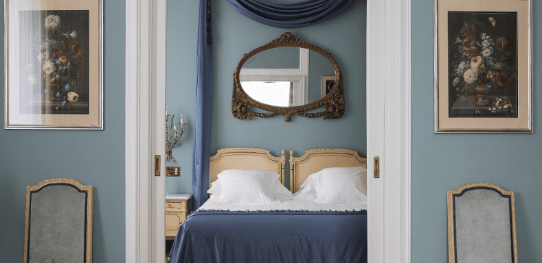 Blue bedroom with an ornate mirror and framed still-life paintings