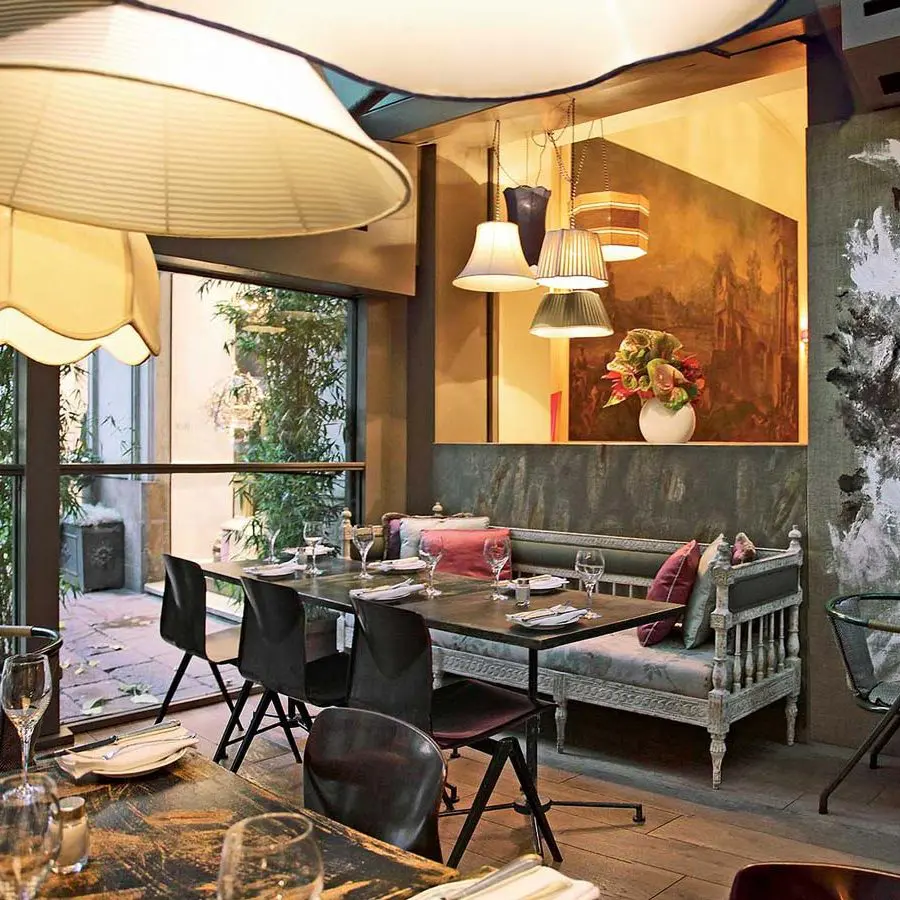 Restaurant dining area with pendant lamps, a floral painting and a carved bench seat