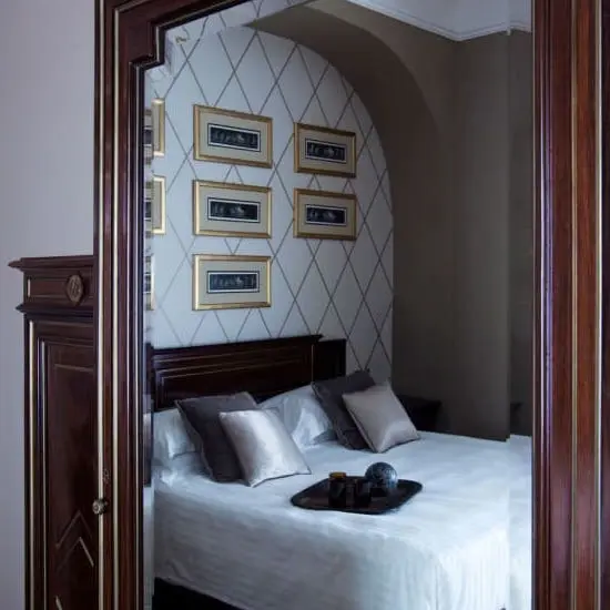Reflection in an arched mirror showing a bed with diamond-patterned wallpaper behind it