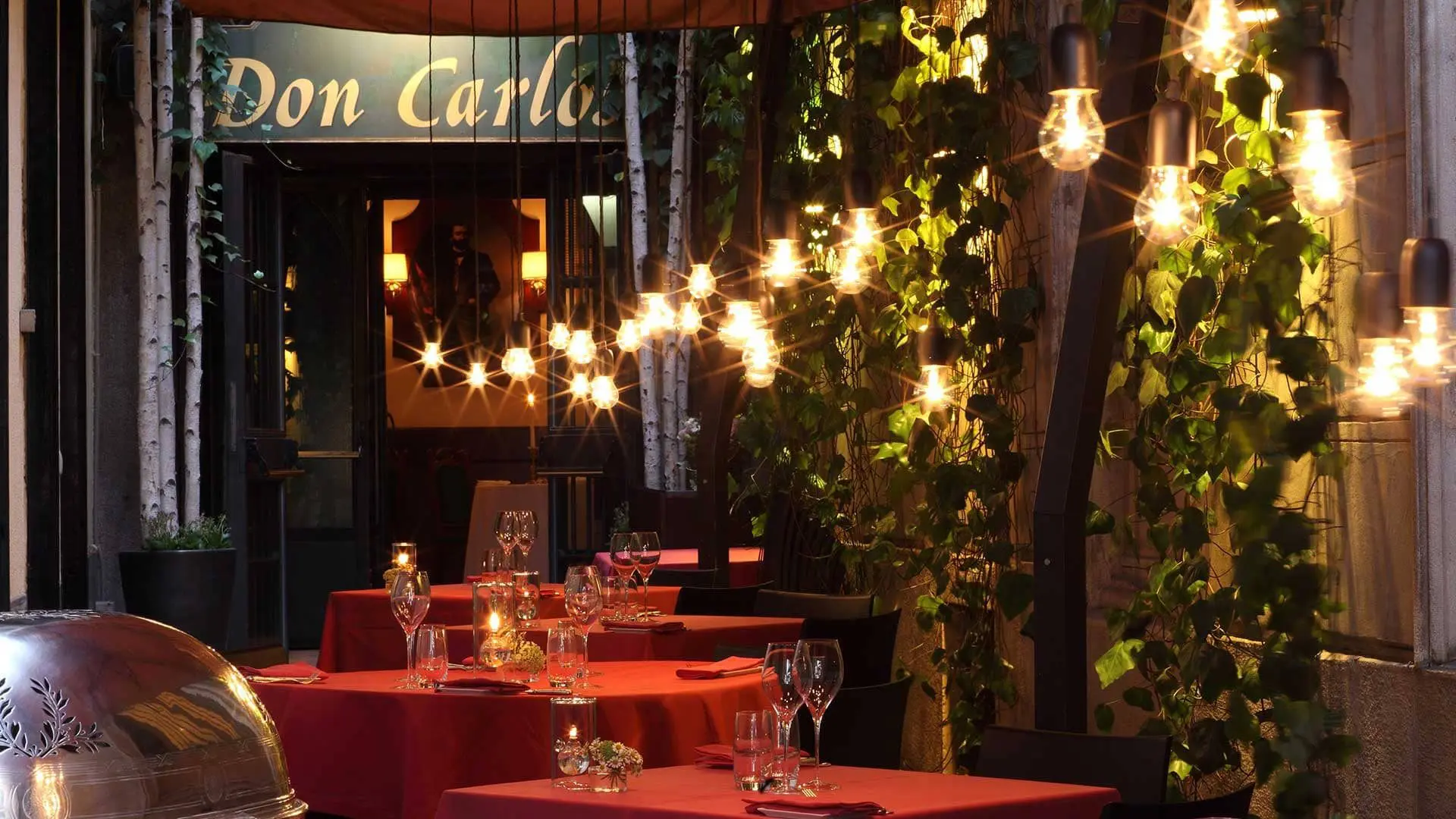 Restaurant terrace with red-clothed tables and string lights under a "Don Carlo" sign