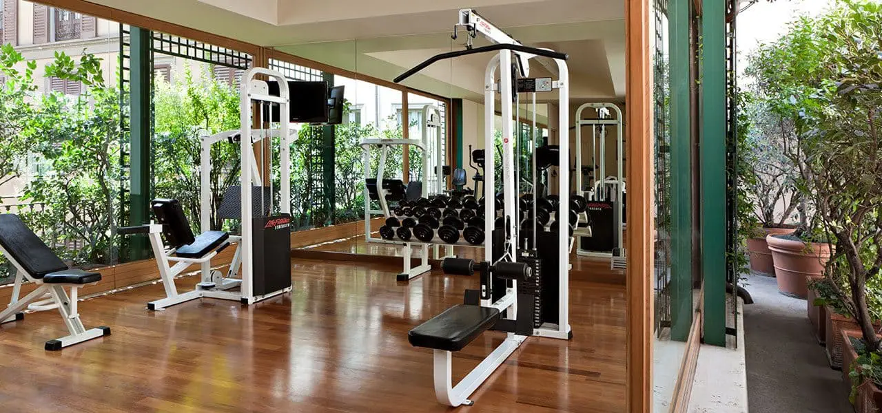 Hotel gym with weight machines, a wood floor and mirrored walls opening to greenery