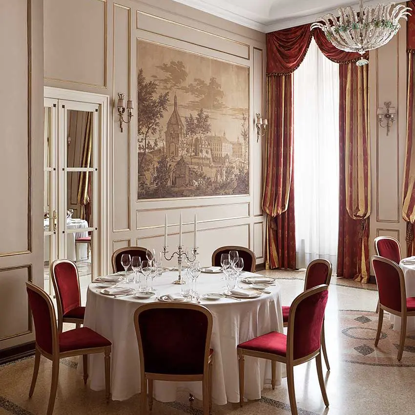 Formal round dining table set for eight beneath a chandelier, with a framed landscape painting