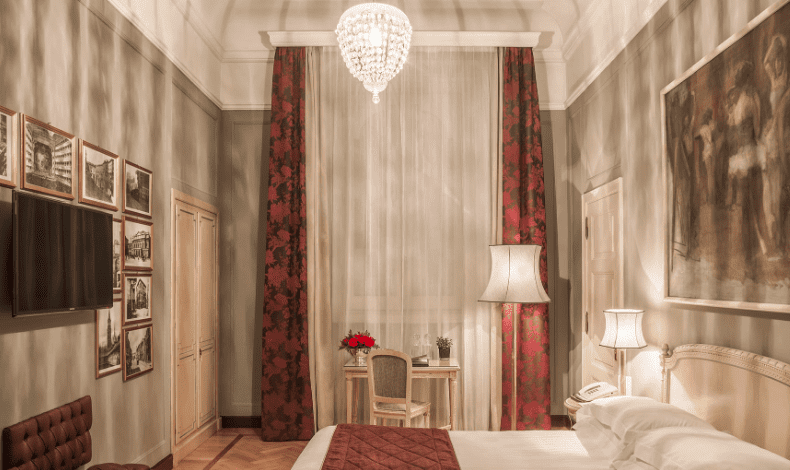 Hotel bedroom with a crystal chandelier, red damask curtains and framed black-and-white photos