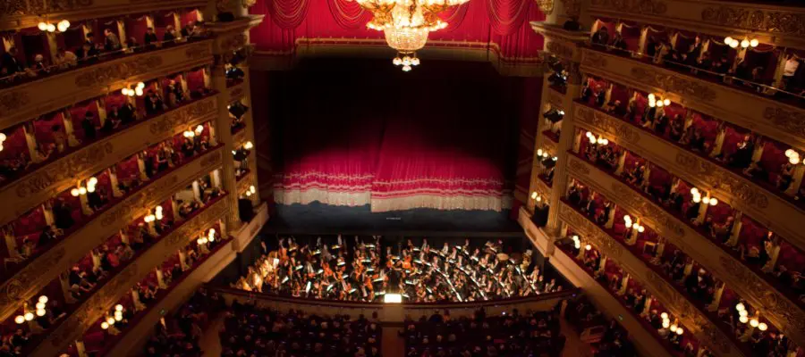 Opera house auditorium filled with audience in tiered boxes overlooking the orchestra and red curtain