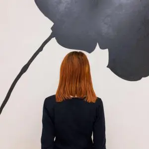Woman with red hair seen from behind standing before a large black floral wall graphic