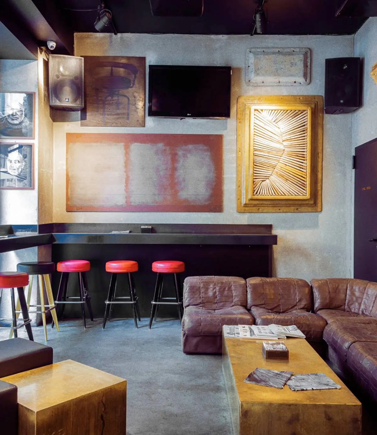 Lounge bar with red stools, leather sofas and framed art on a concrete wall