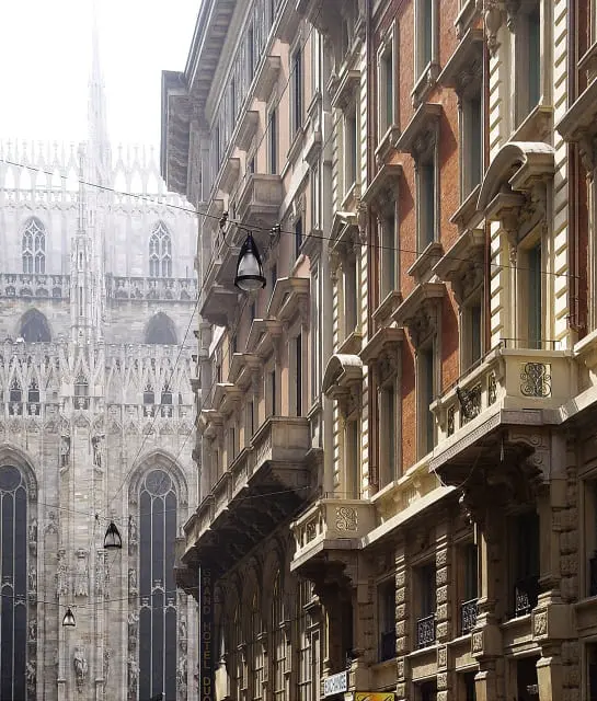 Milan's Gothic cathedral spires seen from a narrow street lined with balconied buildings