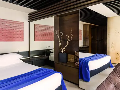 Hotel bedroom with twin beds joined together, a blue throw and mirrored room divider