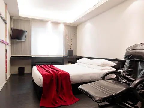 Hotel room with a red throw on the bed, a wall-mounted TV and a black massage chair
