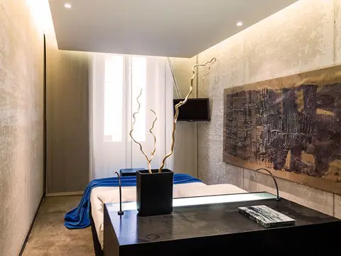 Compact hotel room with a bed, driftwood-style lamp stand and a textured wall panel