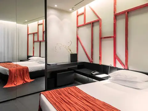 Hotel bedroom with an orange throw, red graphic wall art and mirrored closet doors