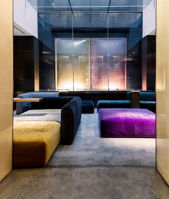 Moody lounge with velvet ottomans behind a glass partition