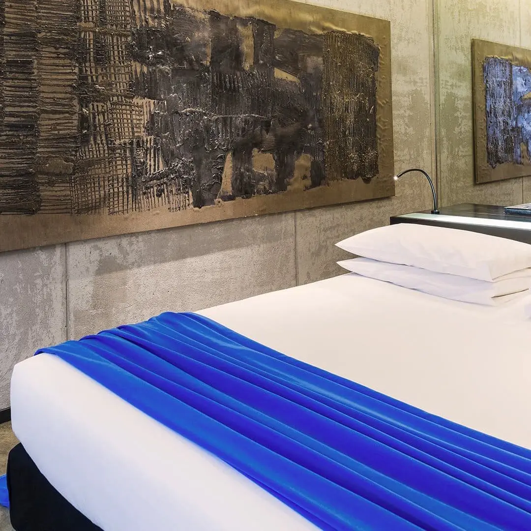 Hotel bed with a blue silk throw beneath abstract metallic wall panels