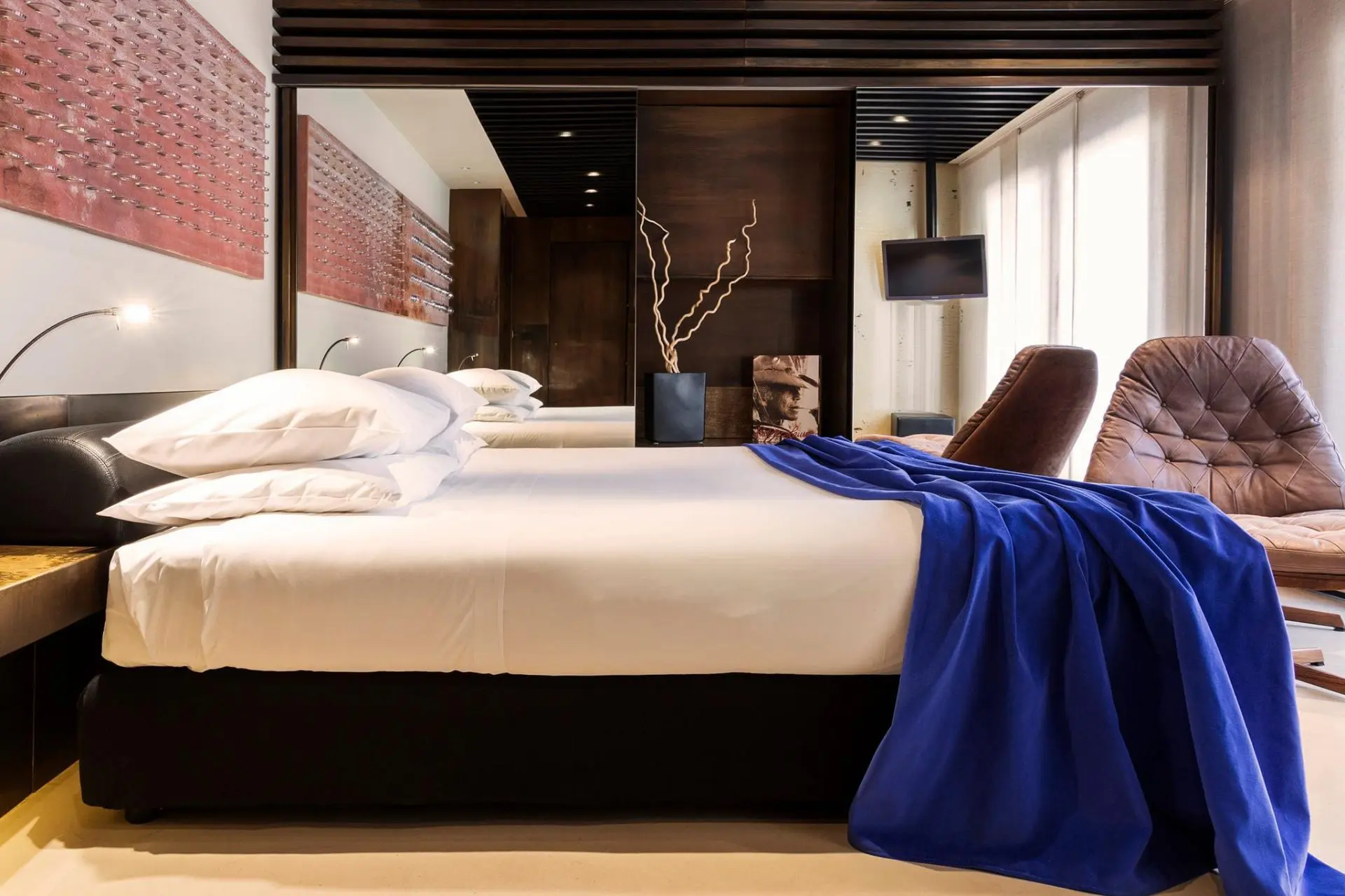 Hotel bed with white linens and a blue throw blanket beside patterned wood panelling