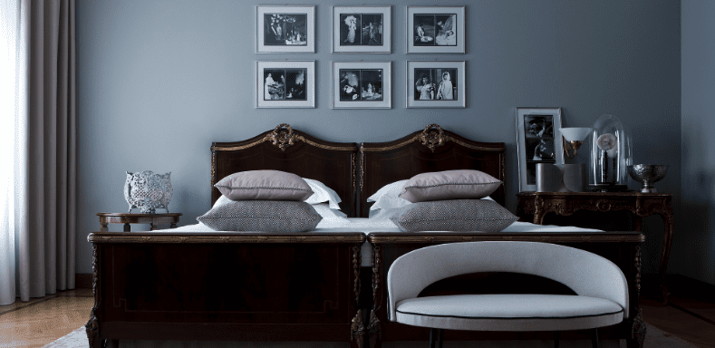 Hotel bedroom with twin dark wood beds, framed photos and a blue-grey wall