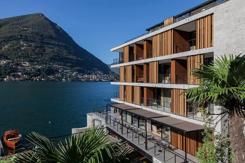 Wood-clad apartment building on a lake shore with mountains in the background