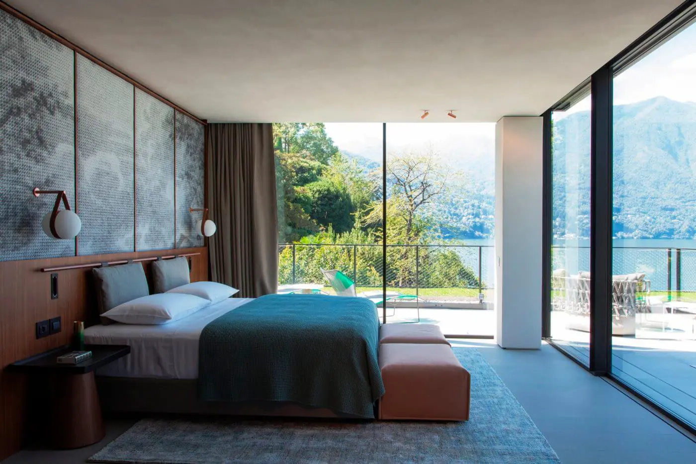 Modern bedroom with floor-to-ceiling windows overlooking a lake and mountains