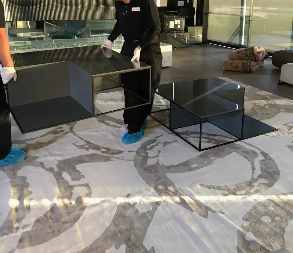 Two gloved workers assembling glass coffee tables on a patterned rug