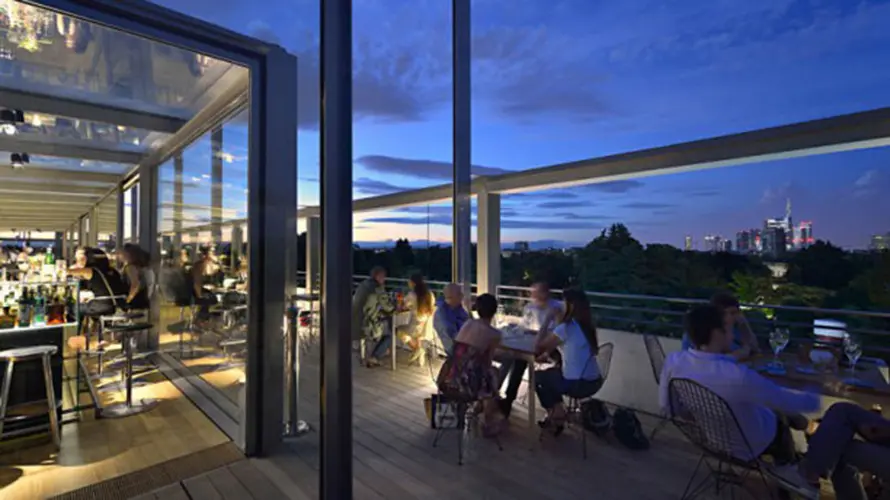 Rooftop terrace at dusk with people dining and a city skyline view