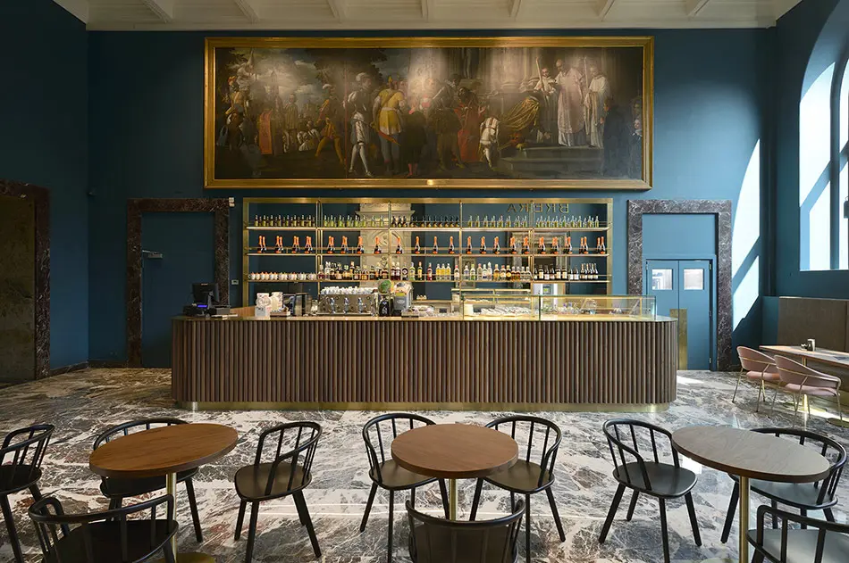 Bar interior with a large painting above shelved bottles and round wood tables