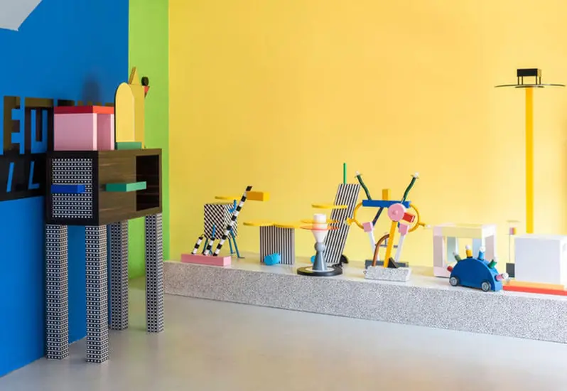 Playful showroom display of colorful geometric objects against blue and yellow walls