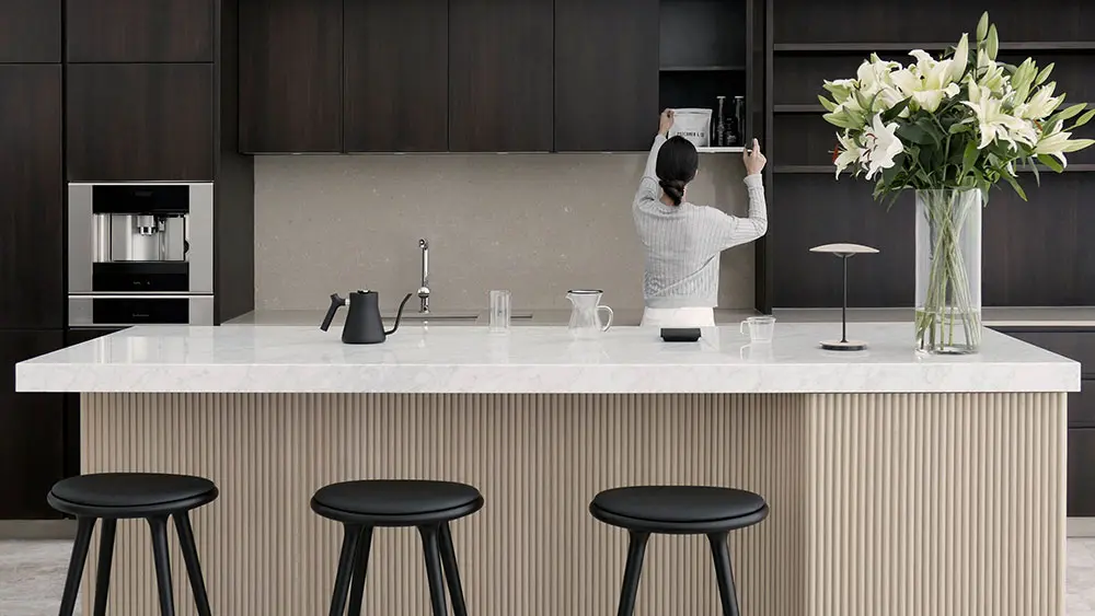 Kitchen with dark cabinetry, a white stone island, black stools and a vase of lilies