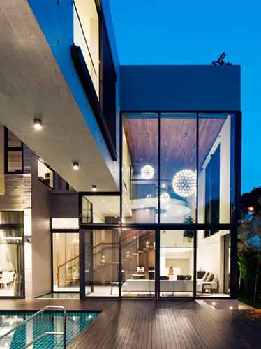 Glass-walled house facade at dusk with a pool deck and hanging spherical lights inside