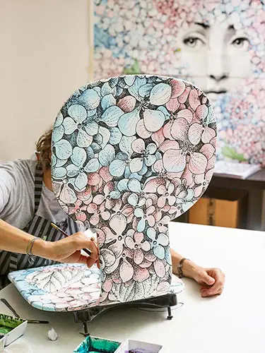 Artisan hand-painting a floral ceramic panel at a workbench