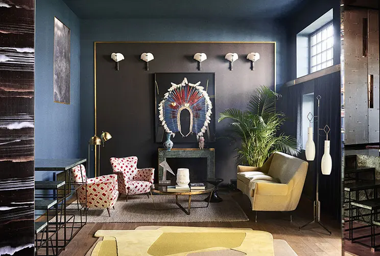 Eclectic living room with dark blue walls, gold sconces, patterned armchairs and a mustard velvet sofa