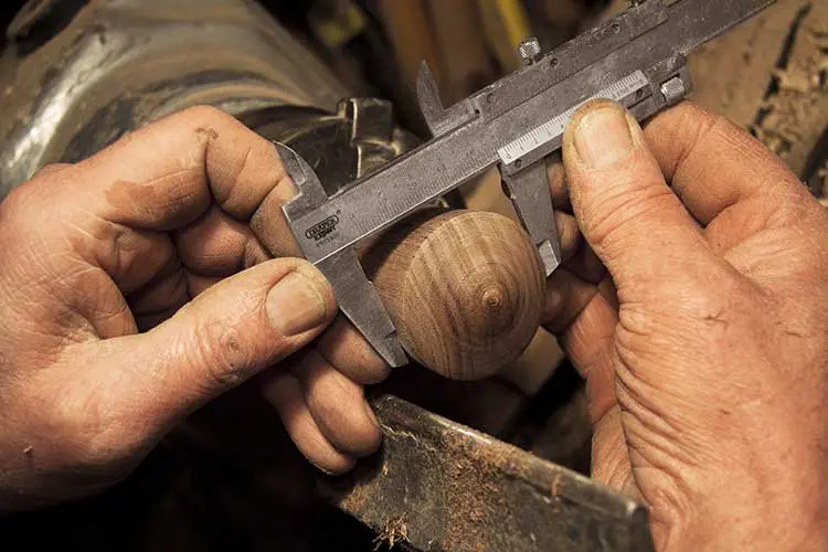 Craftsman measuring a wood ball component with calipers
