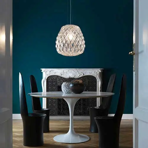 round marble dining table with black sculptural chairs beneath a woven pendant light