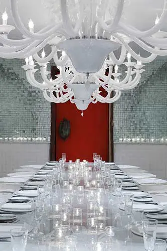 long banquet table set with glassware beneath ornate white glass chandeliers