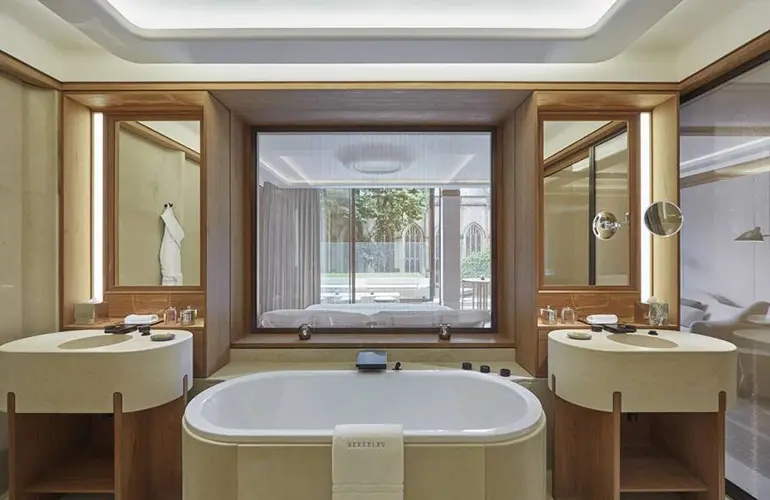 Bathroom with a freestanding tub between two wood vanities and a garden view window