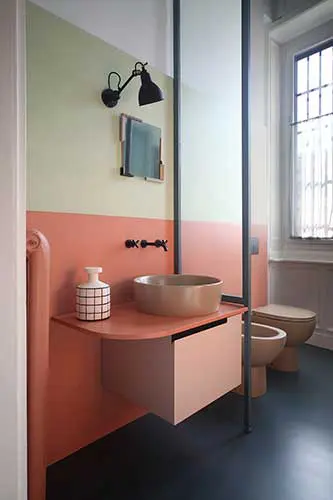 Bathroom with sage green and coral walls, a round wood vanity and black fixtures